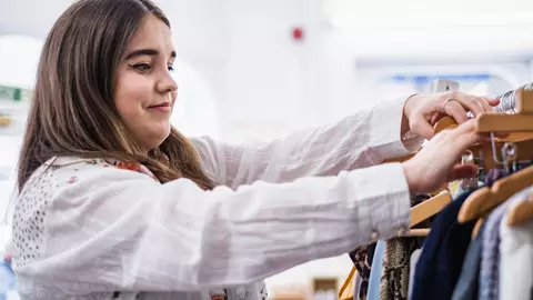A young woman who is volunteering at a Blue Cross charity shop, sorts through a rail of clothing